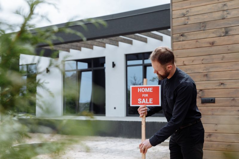 Man placing a home for sale sign outside a modern house for 1785862952